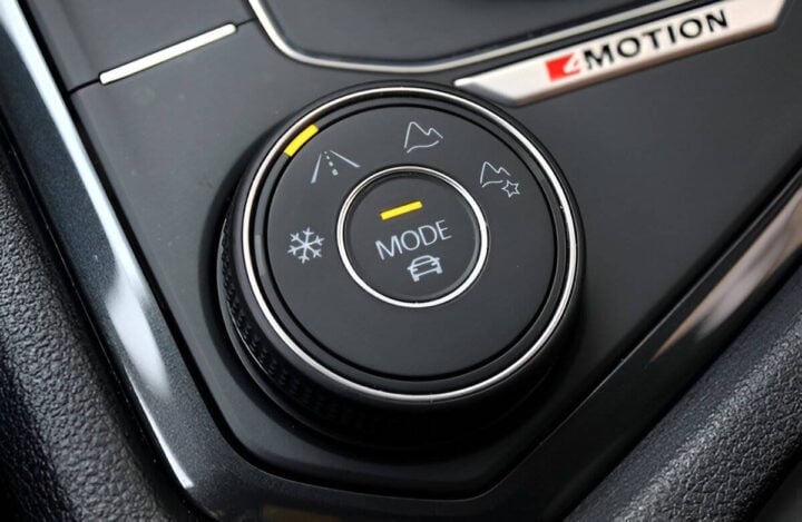 A close-up of a vehicle’s drive mode selector knob, featuring different terrain modes such as snow, road, and off-road settings. The dial is labeled “MODE” and includes icons for various driving conditions. The “4MOTION” badge is visible, indicating an all-wheel-drive system.