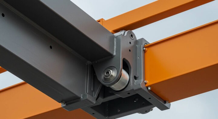 Detailed close-up of a modern industrial crane structure showing the junction between orange and gray steel beams, connected via a precision-engineered pulley and bearing system. The image highlights the high-quality construction and mechanical components used in automated lifting systems.