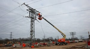 Worker in a safety harness using an EWP boom lift to perform maintenance on high-voltage power lines, demonstrating safe and efficient work at heights in an industrial setting.