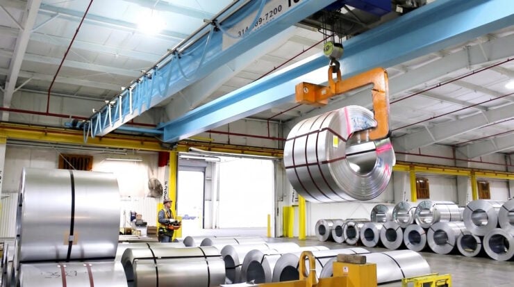 Gantry crane lifting a large steel coil in a warehouse